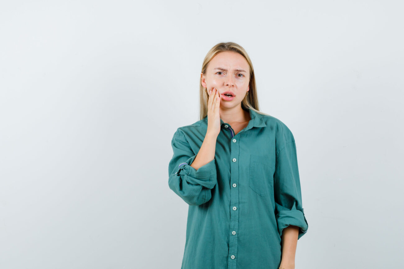 blonde woman suffering from toothache in green shirt and looking uncomfortable , front view